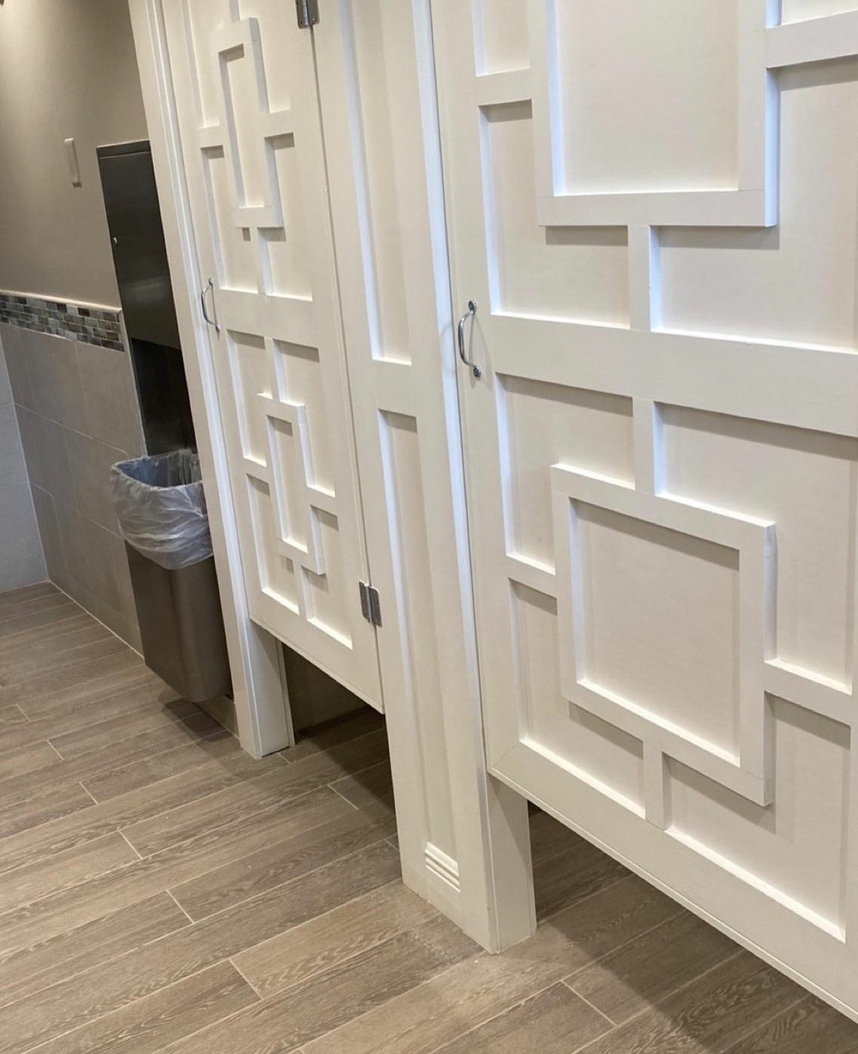 Custom white bathroom stall doors with raised geometric wood trim.