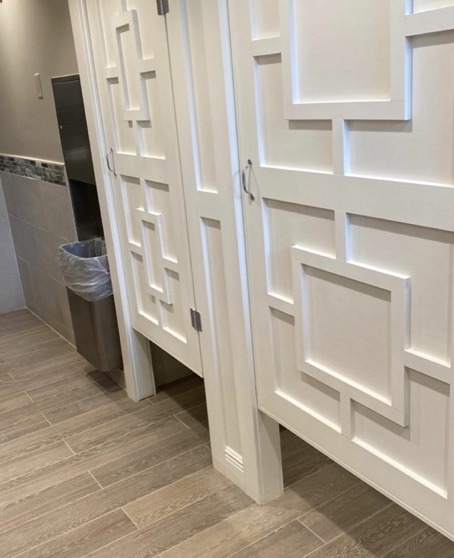 Custom white bathroom stall doors with raised geometric wood trim.